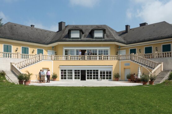 großes gelbes Gebäude mit grüner Wiese in frontaler Ansicht