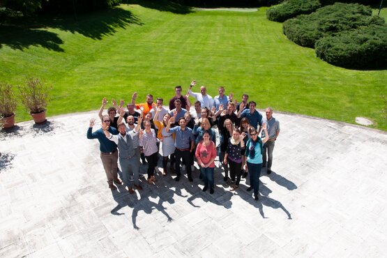 Gruppe von Menschen vor einer grünen Wiese von oben mit Blick in die Kamera