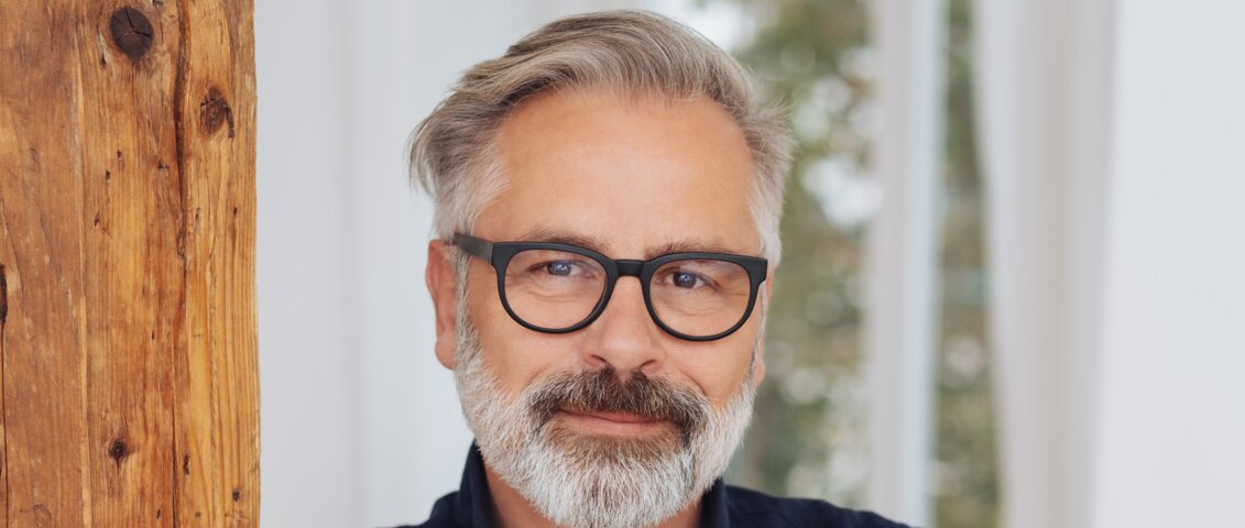 Mann an Holzsäule gelehnt mit Blick in die Kamera