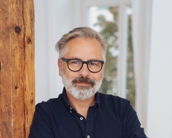 Mann an Holzsäule gelehnt mit Blick in die Kamera