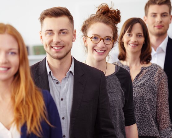 Fünf Mitarbeitende hintereinander aufgestellt von schräg rechts fotografiert mit Blick in die Kamera